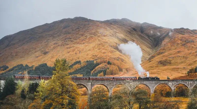 Jacobite steam train crossing the Glenfinnan Viaduct against autumn mountainsides